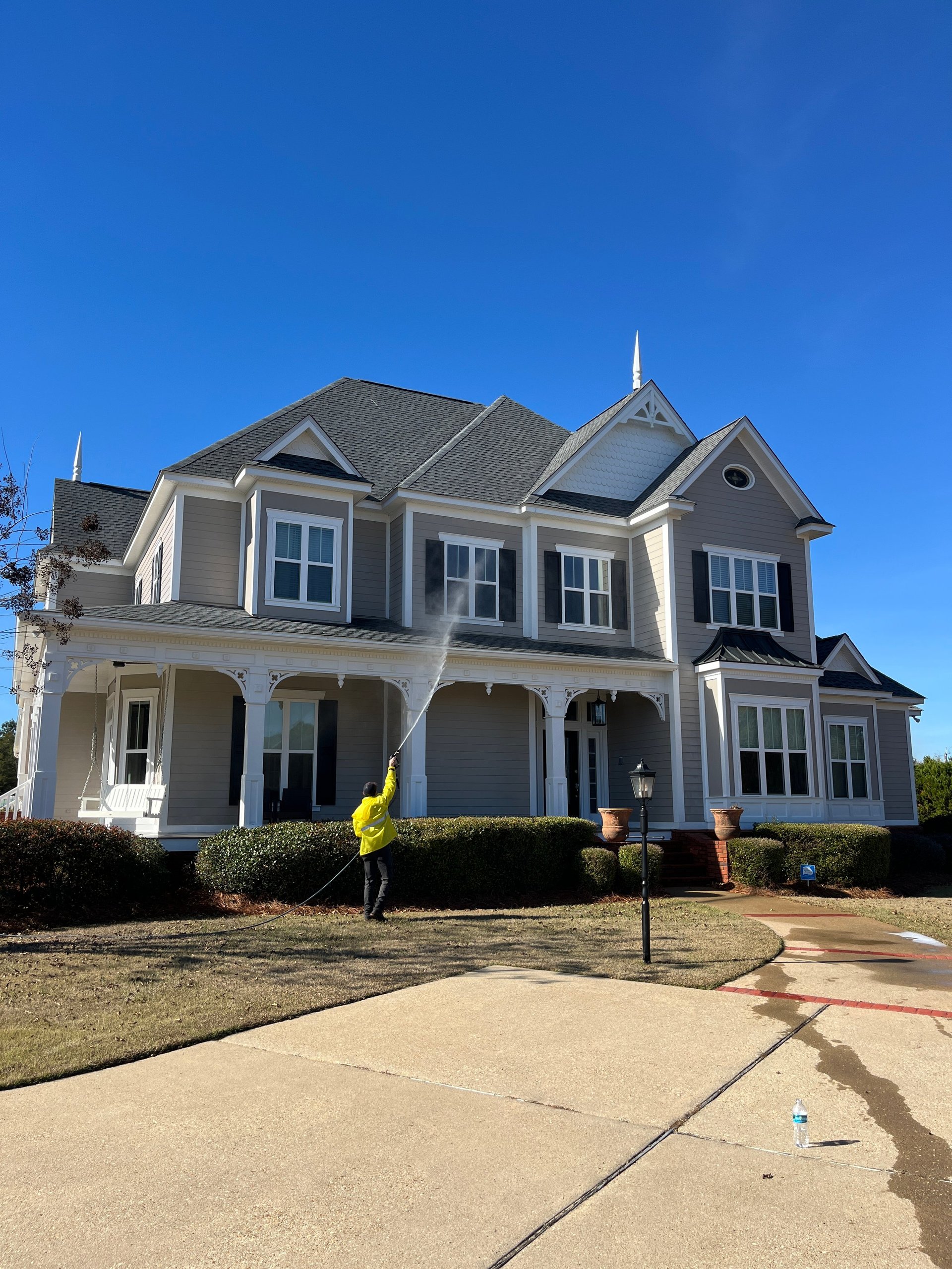 Large two-story colonial-style home with gray roof and front porch under a clear blue sky